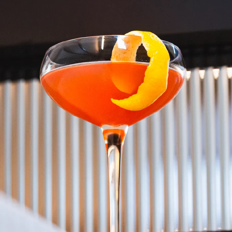 A bright orange cocktail in a coupe glass with a garnish of lemon