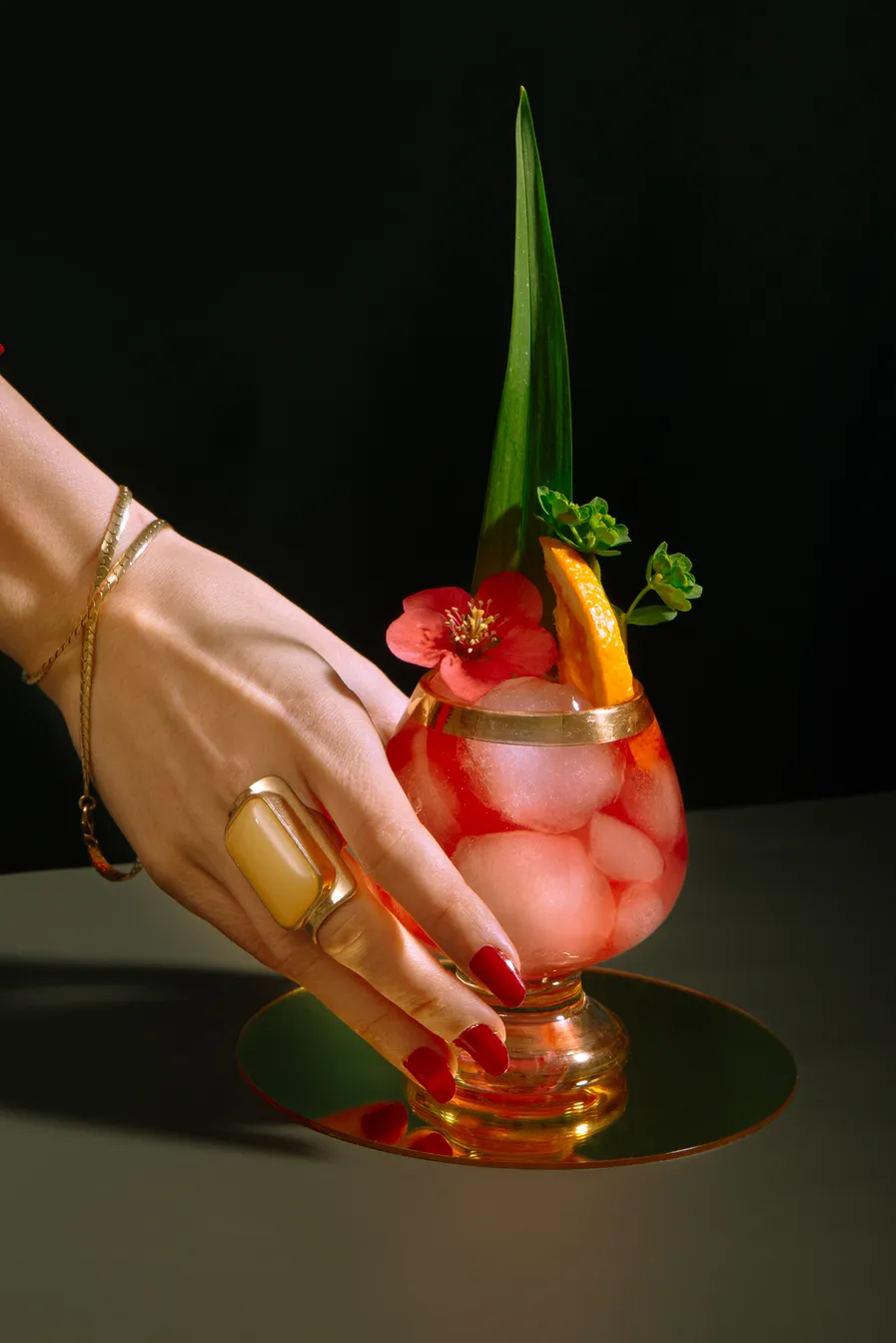 A woman holding an ornately garnished red cocktail