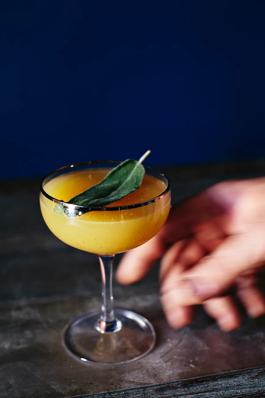 A creamy yellow cocktail garnished with a safe leaf